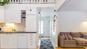 Cocina moderna con armarios blancos, un refrigerador y un microondas. En la sala de estar, hay un sofá marrón con una alfombra estampada.