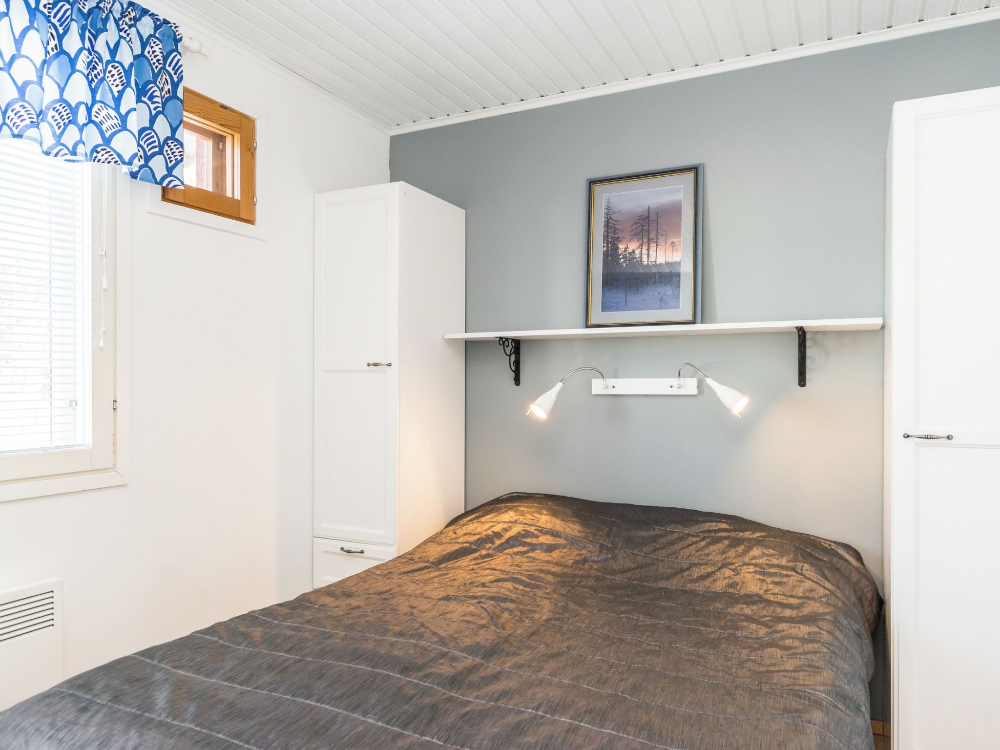 Una camera da letto con un letto, un armadio, uno scaffale con una cornice e una finestra con persiane.