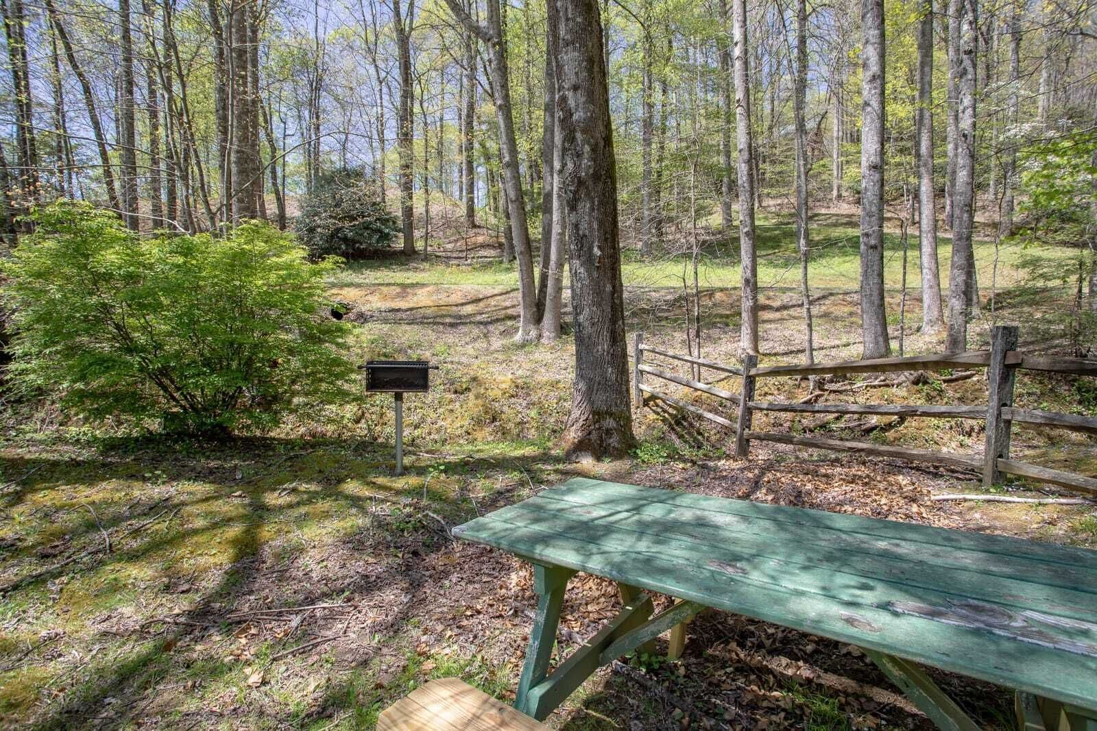 Una mesa de picnic en un área boscosa con una valla de madera y un cartel.
