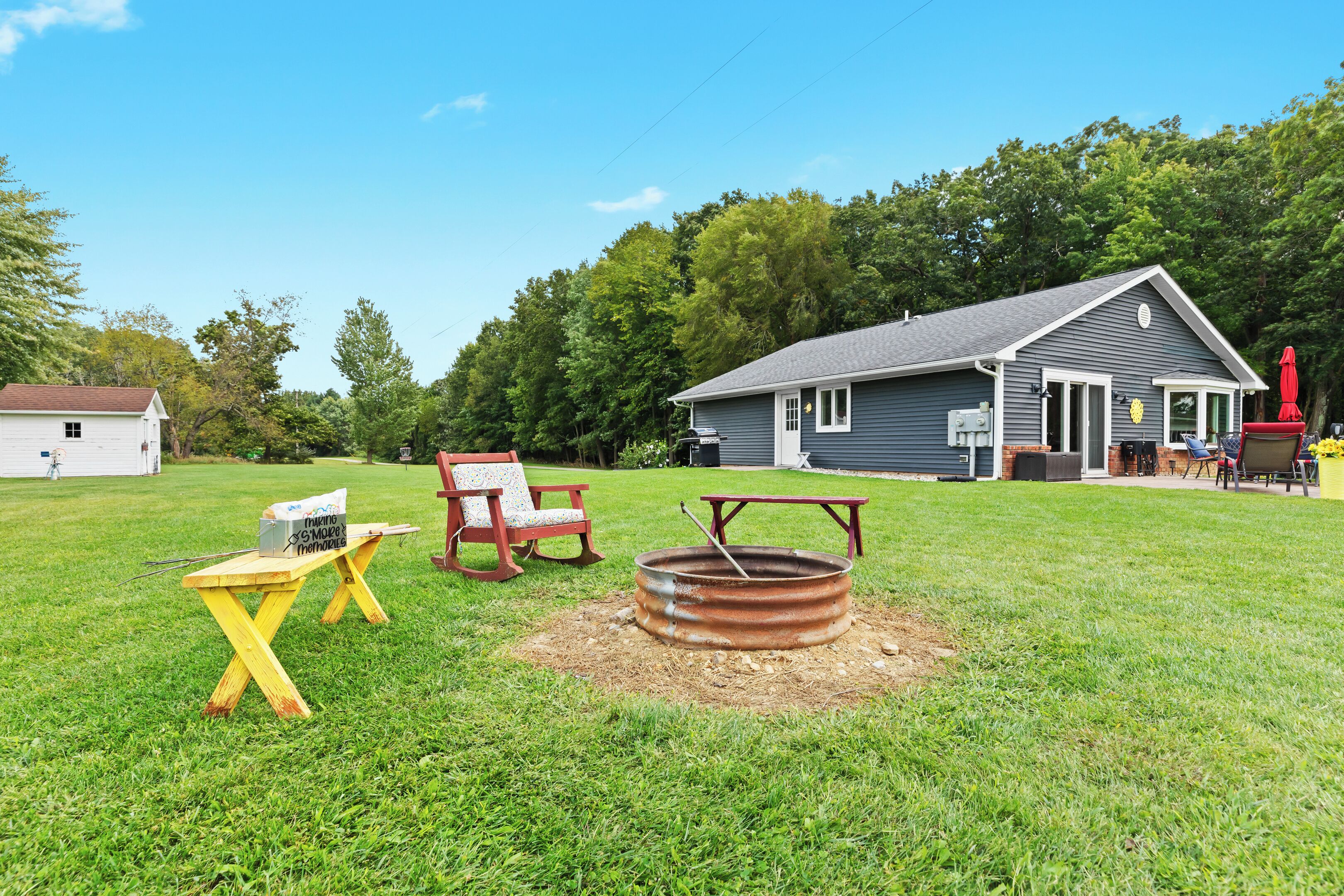 A backyard with a metal fire pit, a wooden table, and two chairs.