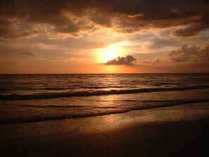 A sunset over the ocean with waves on the shore.