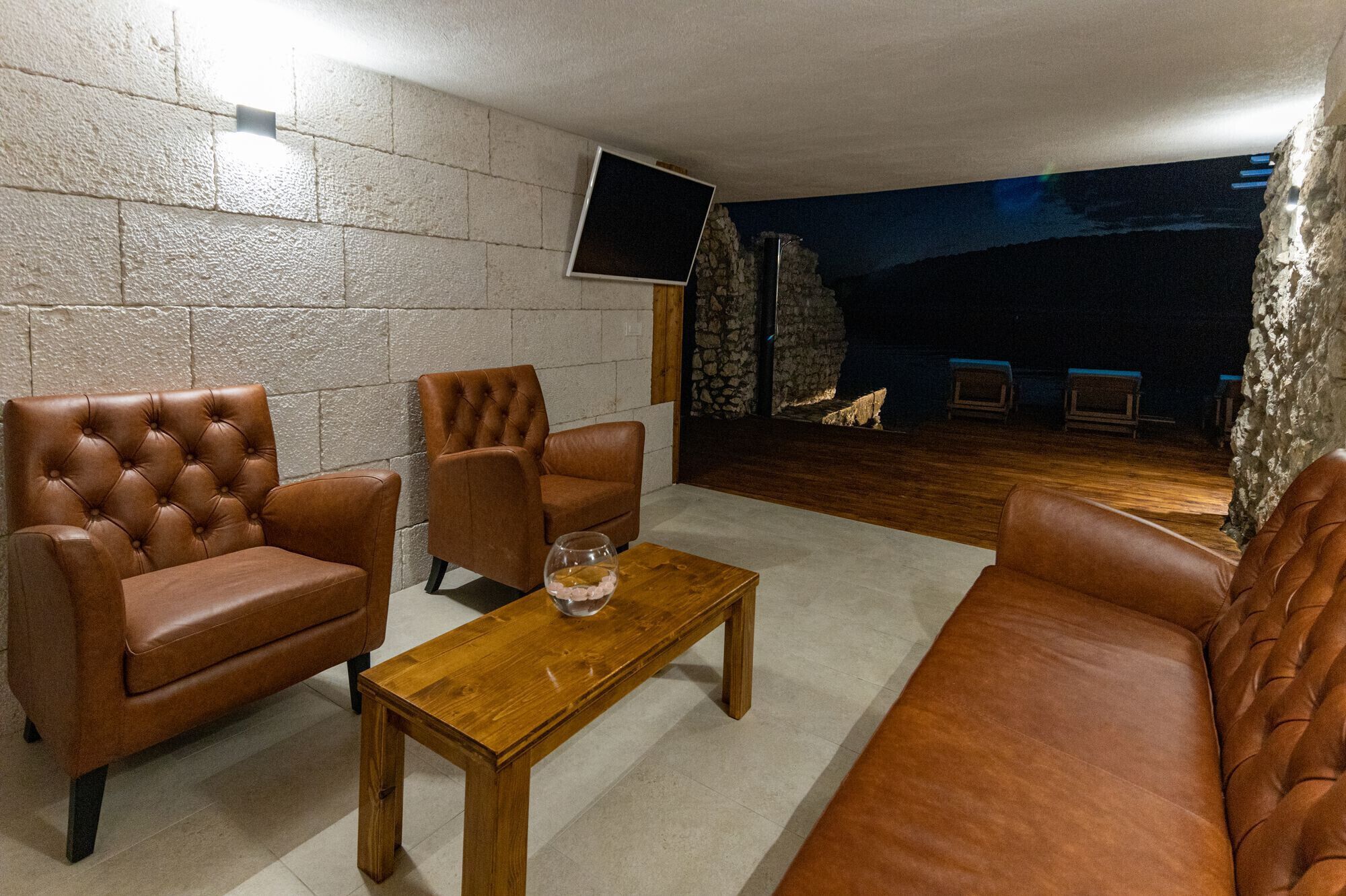 A living room with leather sofas, a wooden coffee table, and a stone wall.