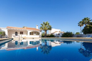 A poolside view of a white building with a tiled roof, surrounded by palm trees and a clear blue sky. - Villa Gondola by Costa CarpeDiem (Alicante)