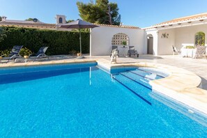 A clear blue swimming pool with lounge chairs and a small table.