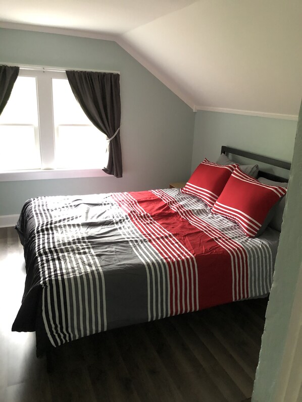 A bedroom with a bed, a window with curtains, and a wooden floor.