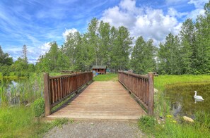Cross a serene bridge to a secluded cabin nestled among lush greenery and a tranquil pond.