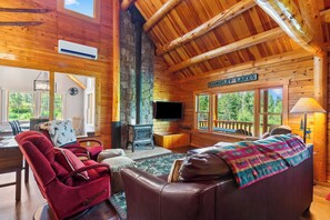A log cabin interior with a stone fireplace, a television, a red recliner, a brown leather sofa, and a sign reading "Rangley Lakes".