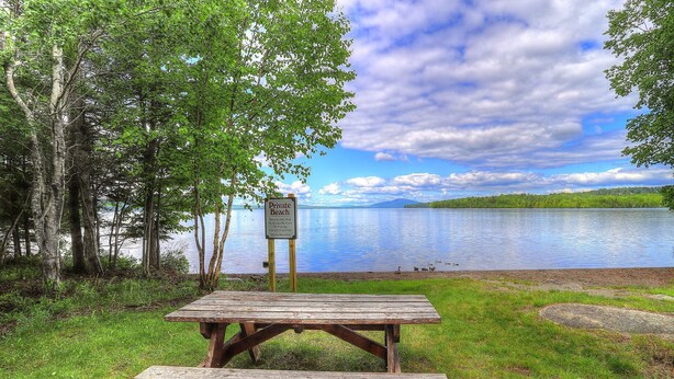A picnic table and bench by a lake with a sign indicating it is a private beach. - Lakehouse Condo 3B | Shared Beach Access on Rangeley Lake (Rangeley)