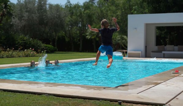 A swimming pool with a person jumping into the water, surrounded by a grassy area and trees.