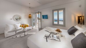 Quarto de hotel moderno com cama, sofá, mesa de jantar e vista para o mar.