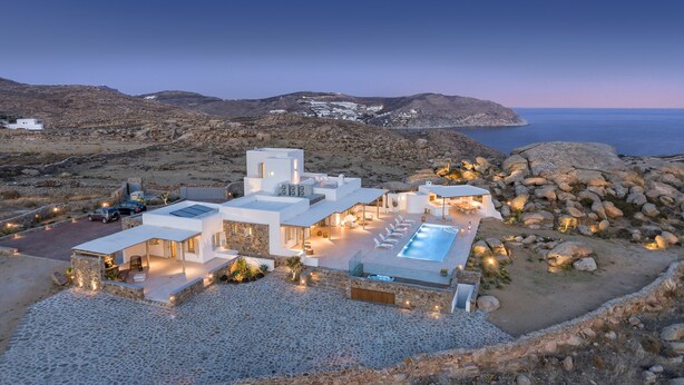 Uma villa moderna com piscina, caminhos de pedra e vista para o mar.