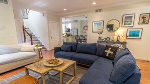 A living room with a sofa, a coffee table, and a brown ottoman. There is a staircase leading to another room.