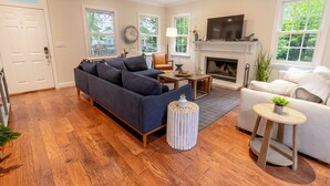 A living room with a dark blue sofa, a white armchair, a round wooden coffee table, and a fireplace.