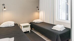 A hotel room with two single beds, a small white nightstand, a white lamp, and a window with blinds. - Skivillas paljakka 1. (3mh) by Interhome (Puolanka)