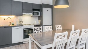 A modern kitchen with grey cabinets, a microwave, a stove, and a dishwasher. There is a dining table with white chairs. - Skivillas paljakka 1. (3mh) by Interhome (Puolanka)