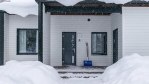 A snow-covered house with a front door, two windows, and a blue shovel on the porch. - Skivillas paljakka 1. (3mh) by Interhome (Puolanka)