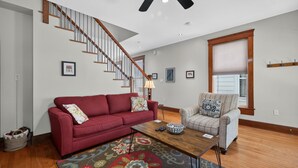 A living room with a red sofa, a patterned rug, a wooden coffee table, a striped armchair, and a staircase with wooden railings. - Fins Up home- Park Views, Close to Beach, Shops (Cape Charles)