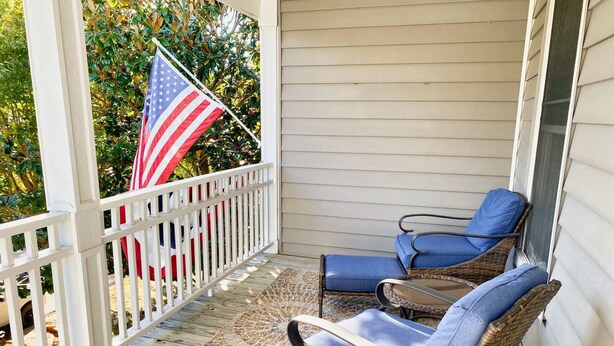 Een veranda met twee rieten stoelen, een vloerkleed met patroon en een Amerikaanse vlag.
