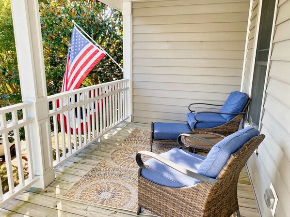 A porch with two wicker chairs, a patterned rug, and an American flag. - Fins Up home- Park Views, Close to Beach, Shops (Cape Charles)
