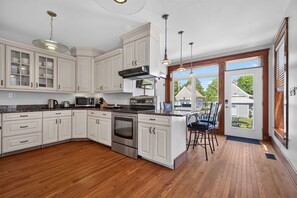 A kitchen with white cabinets, a stainless steel oven, a microwave, and a large island with bar stools. - Fins Up home- Park Views, Close to Beach, Shops (Cape Charles)