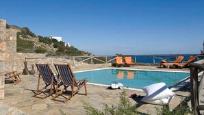 A pool area with lounge chairs, a stone wall, and a view of the sea. - Beautiful 3-bed Sea Front Villa in Agios Nikolaos (Agios Nikolaos)