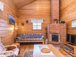 Un interior acogedor de cabaña con detalles de madera, un sofá, un televisor y una chimenea.