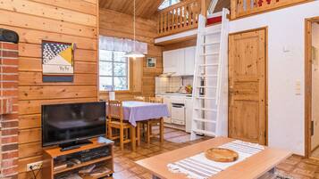Un intérieur de chalet chaleureux et accueillant, avec un téléviseur, une table à manger et un coin cuisine.