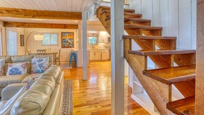 Un amplio salón con una escalera de madera, un sofá de cuero y una cocina al fondo.