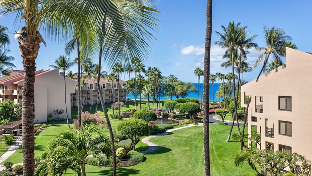 Un resort con un césped bien cuidado, palmeras y vista al océano.