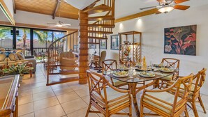Un comedor amplio con escalera de madera, mobiliario de mimbre y vistas al exterior.
