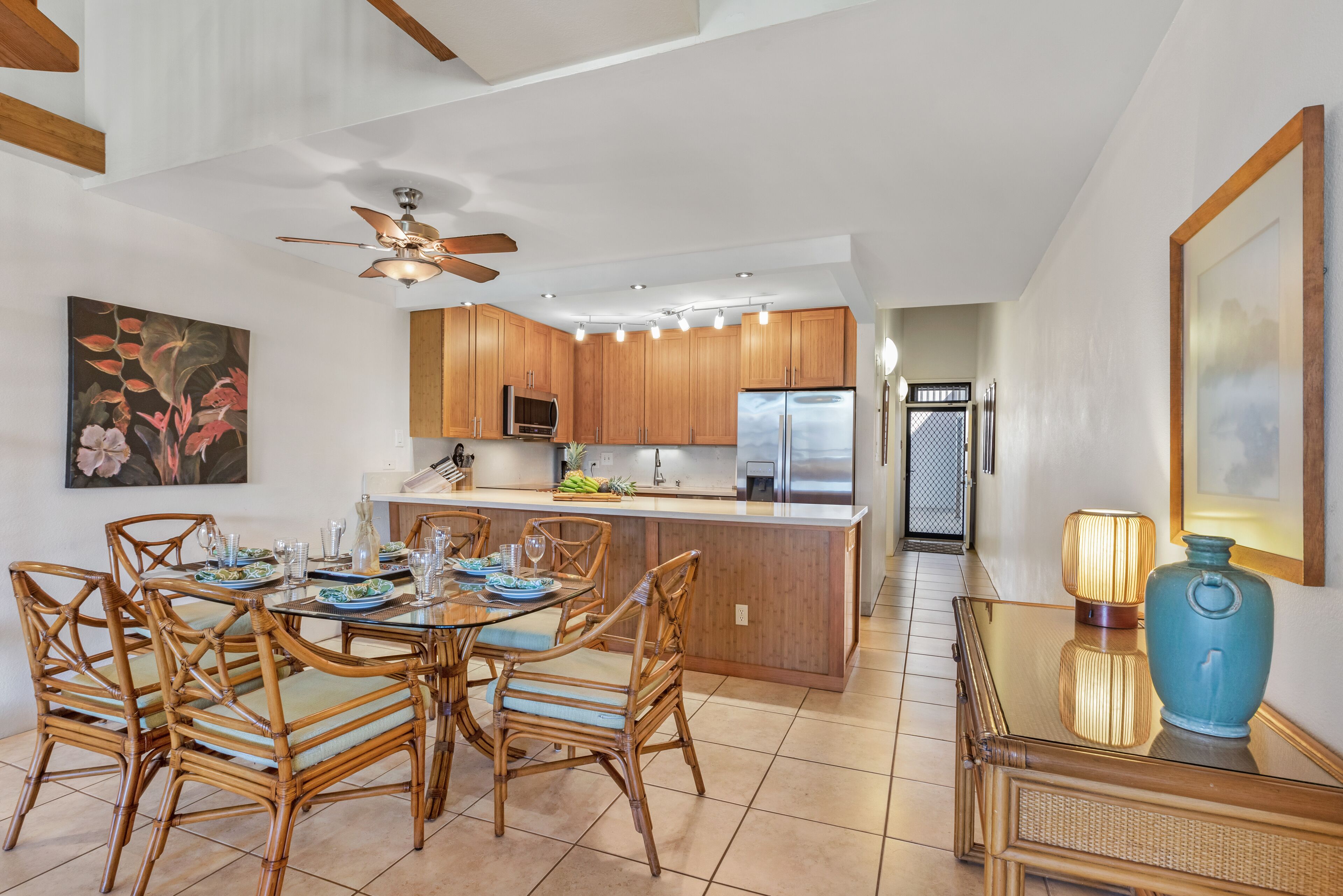 A modern kitchen with wooden cabinets, a central island, and a dining area with wicker chairs.