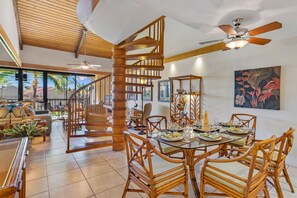 A spacious dining area with a wooden staircase, wicker furniture, and a view of the outdoors.