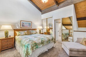 A bedroom with a large bed, two bedside tables with lamps, a mirror, and a door leading to another room.