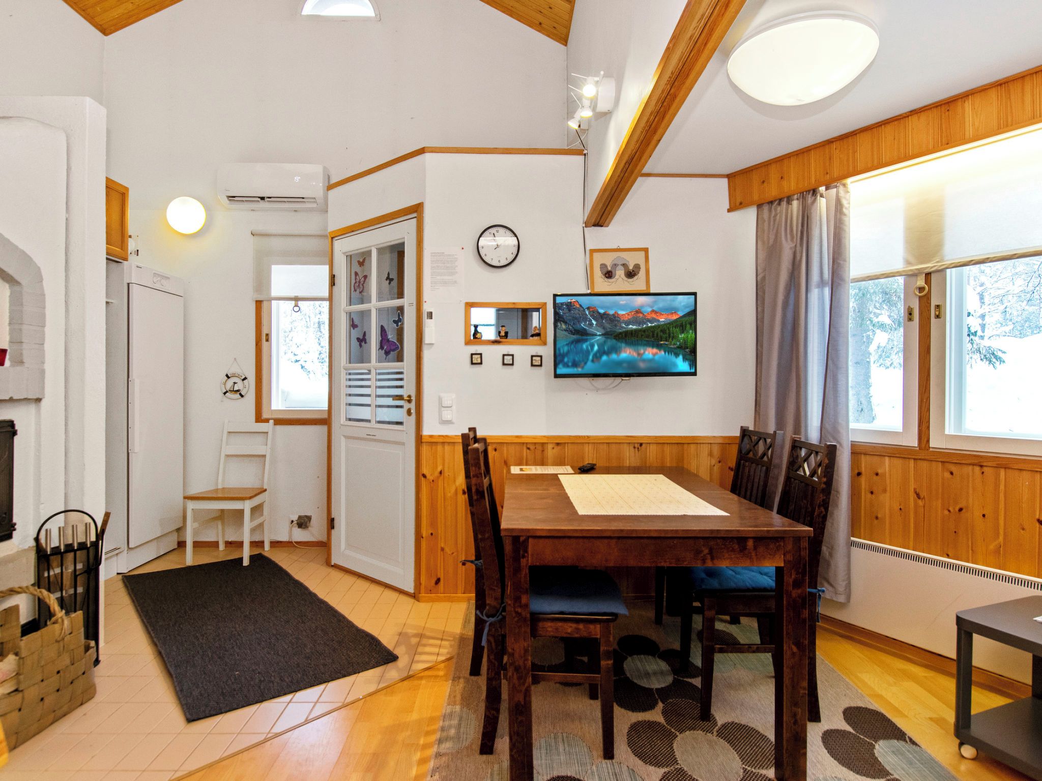 Un coin repas avec une table et des chaises en bois, un tapis noir et une fenêtre avec des rideaux.