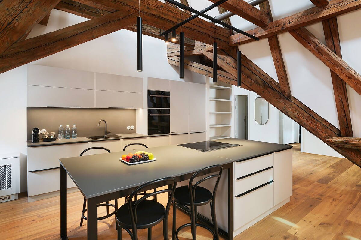 A modern kitchen with a central island, white cabinetry, and exposed wooden beams.
