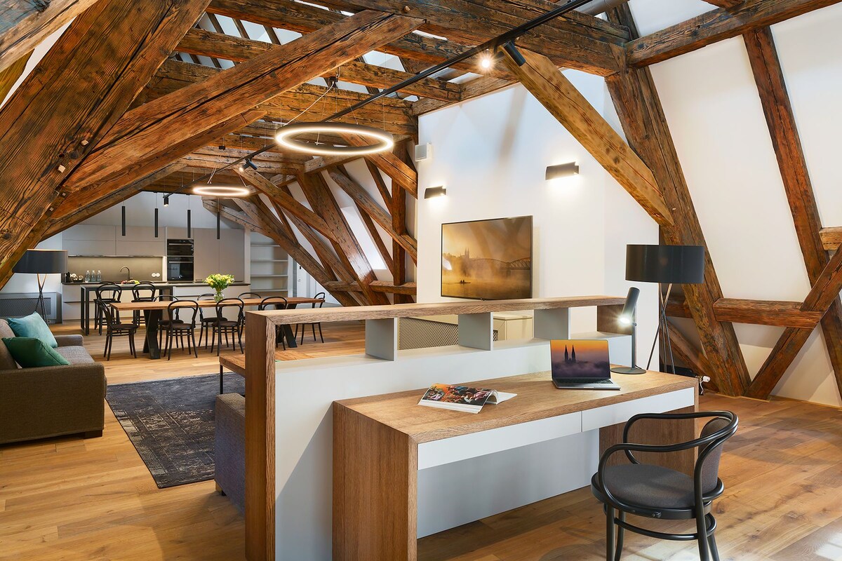 A modern loft with exposed wooden beams, a central dining area, and a workspace with a laptop.