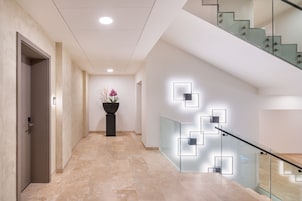 A modern hallway with a glass railing, a potted plant, and a geometric light fixture.