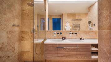 Un baño moderno con dos lavamanos, cabina de ducha de vidrio y tocador de madera.