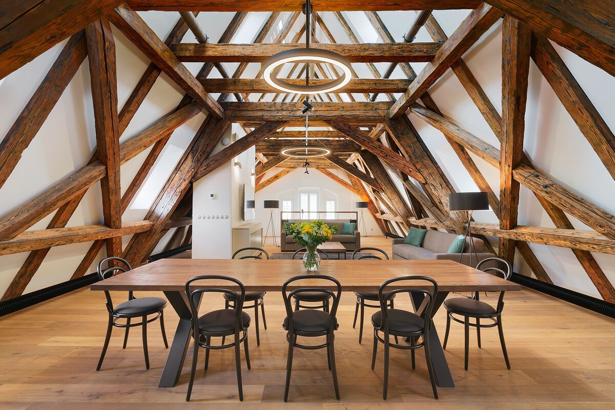 A dining area with a wooden table and chairs, a chandelier, and exposed wooden beams.