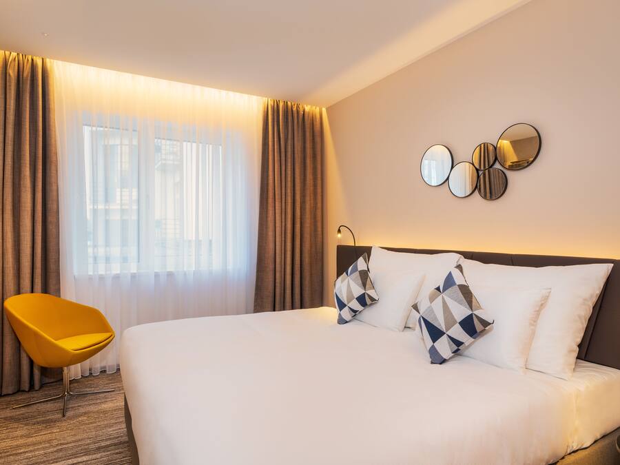 Ein Hotelzimmer mit einem großen Bett, einem gelben Sessel und einer Wand mit runden Spiegeln.