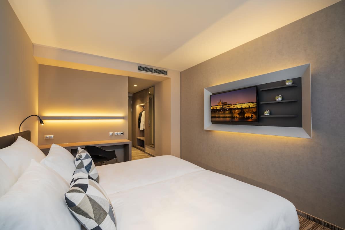 A hotel room with a bed, a TV mounted on the wall, a desk, and a mirror.