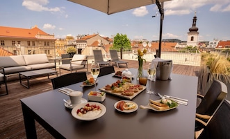 A rooftop dining area with a table set for a meal, outdoor seating, and a view of the cityscape.