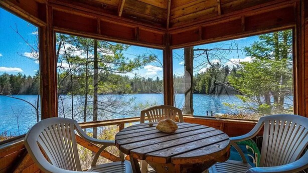 Una baita di legno con un tavolo rotondo e quattro sedie, con vista su un lago e una foresta.