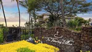 Eine Steinsäule mit dem Schild "The Fairway Villas", umgeben von gelben Blüten und Palmen.