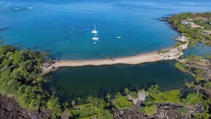 Eine Luftaufnahme einer Küstenlandschaft mit klarem, blauem Wasser, einem Sandstrand und üppigem Grün.