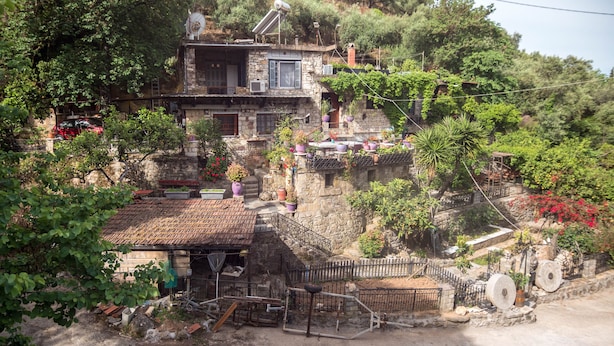 A rustic stone building with a tiled roof, surrounded by lush greenery and potted plants. - Kitries Home (West Mani)
