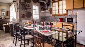 A dining area with a glass table, wooden chairs, and a kitchen in the background. - Kitries Home (West Mani)