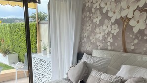 A bedroom with a large bed, a view of the outdoors, and a decorative wall. - Apartment with large terrace and garden 300M from the beach (Mandelieu-la-Napoule)