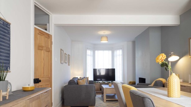 A modern living room with a grey sofa, wooden flooring, and a flat-screen TV.