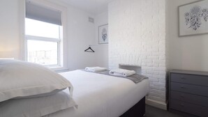 A bedroom with a bed, a dresser, a window, and a brick wall.